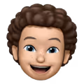 3D animated emoji of a smiling young person with curly brown hair and freckles.